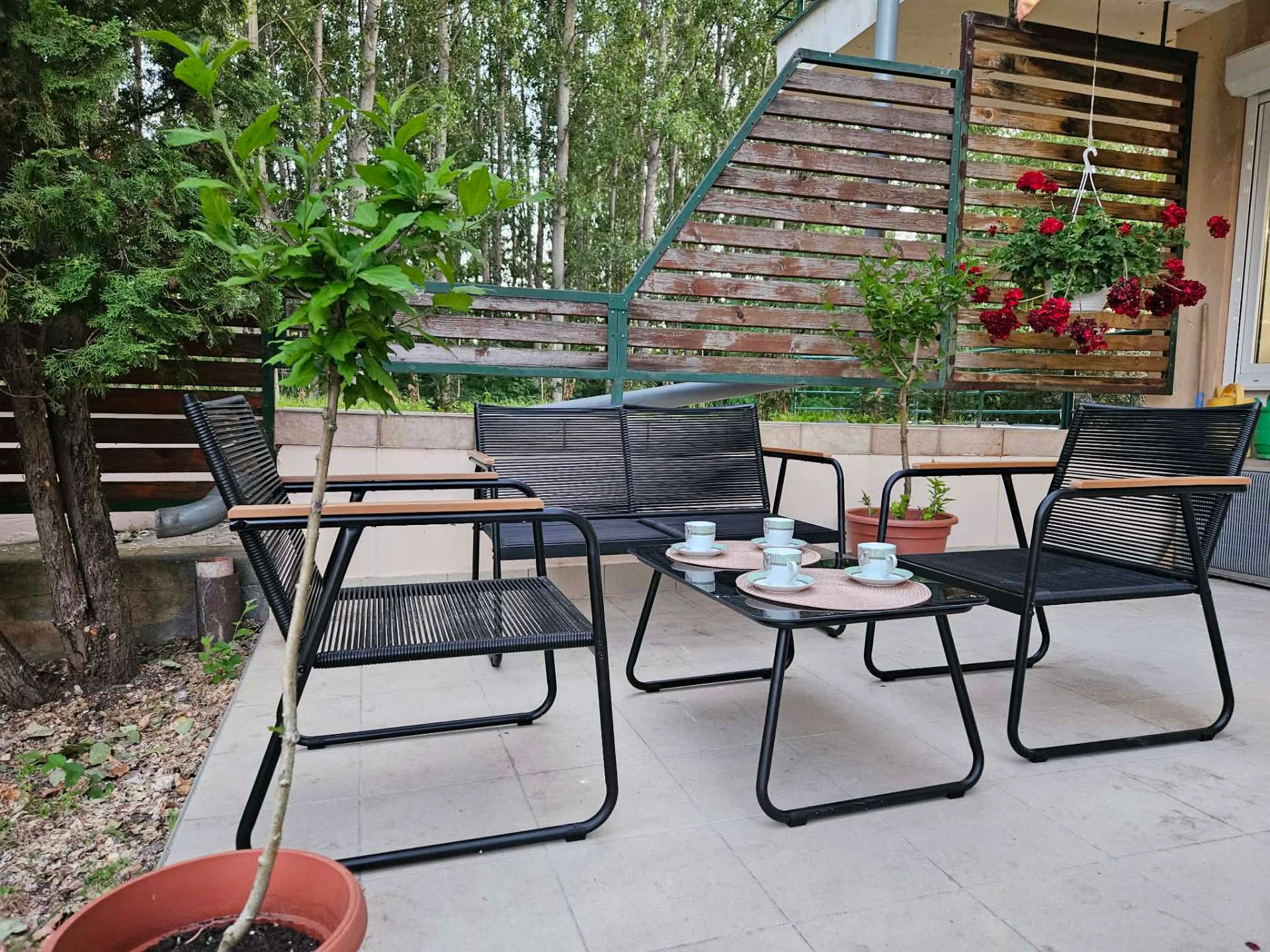 Terasz fekete lounge garnitúrával, kávéskészlettel és muskátlikkal